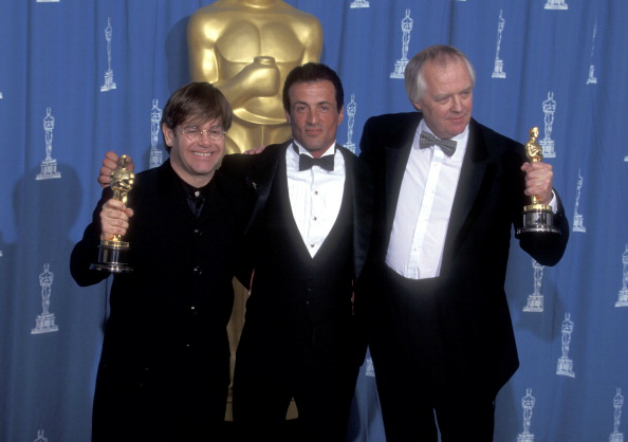 From left: Elton John, Sylvester Stallone (presenter), Tim Rice at Academy Awards, 1995 © Getty Images