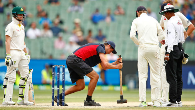 Steve Smith of Australia and bowler Stuart Broad of England look on as the groundsman tries to flatten the bowlers foot marks on the pitch   © Getty Images